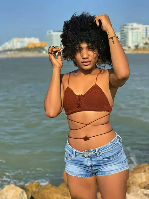 Hot girl with caramel complexion poses on the beach with her hair a mess and her midriff showing.