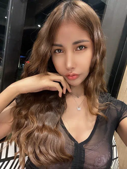 Asian beauty pouts in front of the camera while wearing a sheer black shirt.