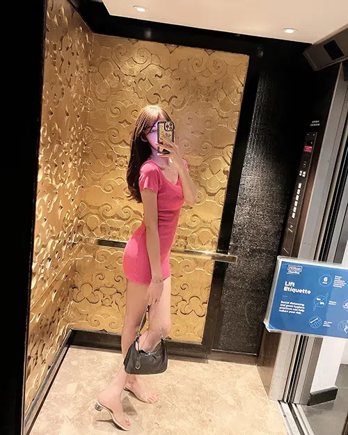 Sexy girl stands in an elevator wearing a pink dress and stops to take a selfie.